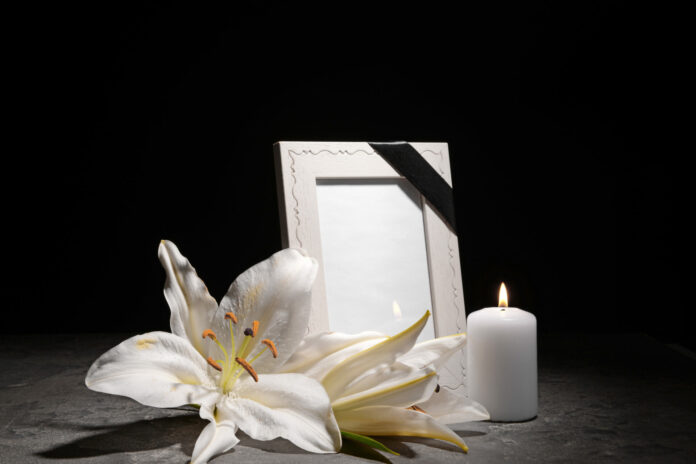 Blank funeral frame, burning candle and flowers on table against
