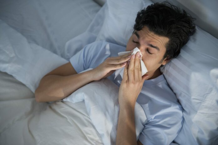 USA, New Jersey, Jersey City, man lying in bed and blowing nose